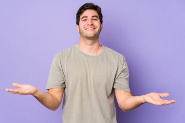 Mor arka planda izole edilmiş genç adam kollarıyla ölçek oluşturuyor, mutlu ve kendinden emin hissediyor..