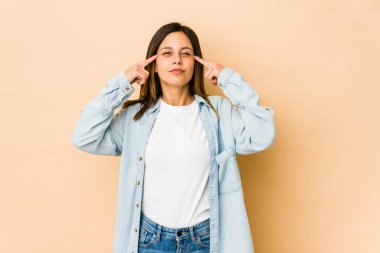 Bej arka planda izole edilmiş genç bir kadın bir göreve odaklanmış, işaret parmaklarını işaret ediyor..