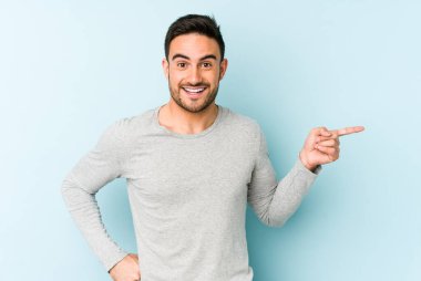 Mavi arka planda izole edilmiş genç beyaz adam işaret parmağıyla işaret ederek gülümsüyor..