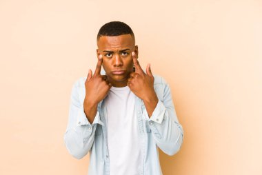 Bej arka planda izole edilmiş genç latin adam bir göreve odaklanmış, işaret parmaklarını işaret ediyor..