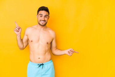 Sarı arka planda mayosu olan genç beyaz bir adam farklı kopya alanlarına sürüklenen genç beyaz bir adam, onlardan birini seçiyor, parmaklarıyla gösteriyor..