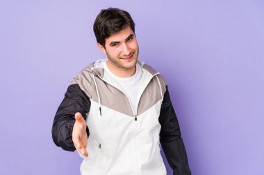 Mor arka planda izole edilmiş genç bir adam kameraya elini uzatarak selam veriyor..