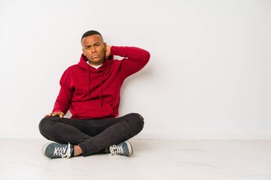 Yerde oturan genç latin adam sabit yaşam tarzından dolayı boyun ağrısı çekiyor..