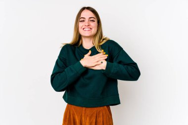 Beyaz arka planda soyutlanmış beyaz tenli genç bir kadın gülüyor, ellerini kalbe koyuyor, mutluluk kavramını koruyor..