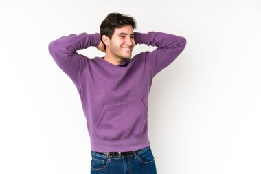 Beyaz arka planda izole edilmiş genç bir adam kendini güvende hissediyor, elleri başının arkasında..