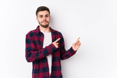 Beyaz arka planda poz veren beyaz tenli genç adam işaret parmağıyla fotokopi alanını işaret ederek şok oldu..