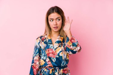 Pijama giymiş genç beyaz bir kadın bir dedikoduyu dinlemeye çalışıyor..