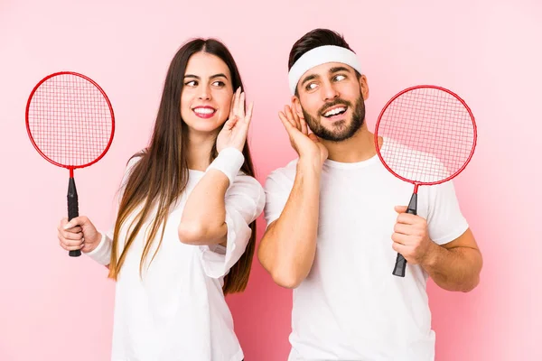 Casal Jovem Jogando Badminton Isolado Tentando Ouvir Uma Fofoca — Fotografia de Stock