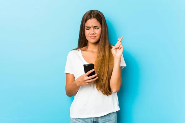 Young Caucasian Woman Holding Phone Crossing Fingers Having Luck — Stock Photo, Image