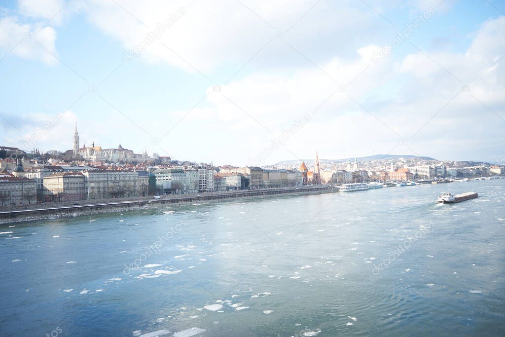 City panorama of Budapest from the Szechenyi chain bridge with ice on the Danube river and a ship