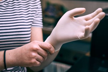 Coronavirus önleme için çizgili tişört giyen bir kız tek kullanımlık plastik eldiven giyiyor.