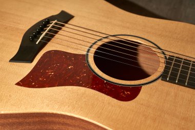 Akustik gitarın ses deliğinin ayrıntıları. Kahverengi ahşap zeminde kırmızı bir pena koruyucu.
