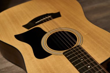 12 telli akustik gitarın ses deliğinin ayrıntıları. Kahverengi ahşap bir zeminde siyah pena koruması var.