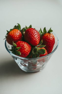 Arka planda büyük bir pencere olan beyaz bir mutfakta cam bir kasede çilek..