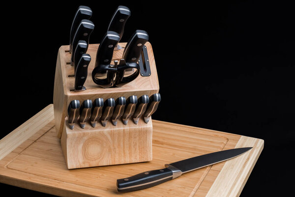 Set of Kitchen knives in a knife block with the chef knife laying on a cutting board, isolated on a black background