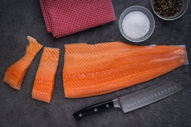 Somon filetosu Santoku bıçağı, tuz, biber ve mutfak havlusuyla kesiliyor.