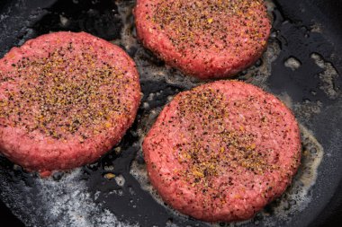 Üç çiğ, baharatlı hamburger, erimiş tereyağının üzerine dökme demir bir tavaya konur ve pişirme işlemini başlatır.