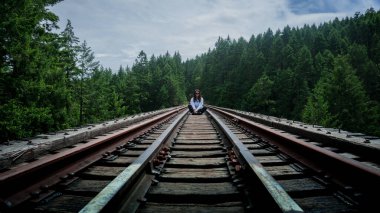 Victoria Kanada 'daki eski demiryolu köprüsünde oturan kız
