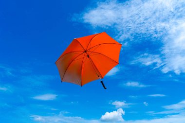 Mavi yaz gökyüzü beyaz kabarık bulutlar ve kırmızı şemsiyeyle 