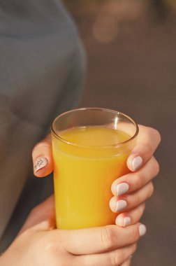 Kız sıcak bir yaz gününde buz portakal suyu içiyor. Kız elinde parlak turuncu bir bardak tutuyor.