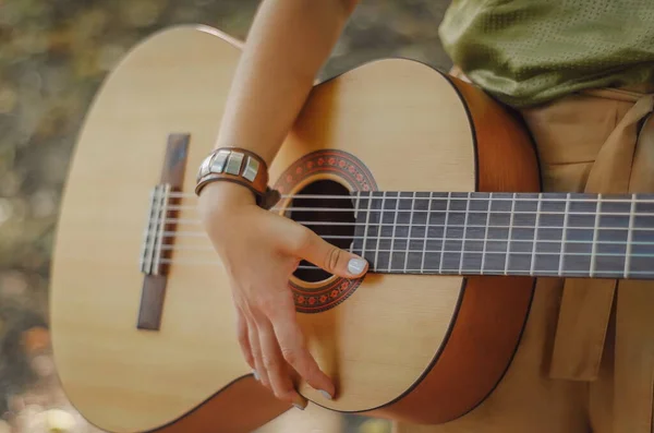 Kız ahşap gitar çalıyor. Gitarda şarkı çalan genç bir kadın..