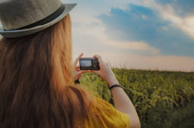 Kırmızı renkli dijital kameralı bir kız bir yaz tarlasının fotoğraflarını çekiyor. Kameranın yakın çekim görüntüsü..