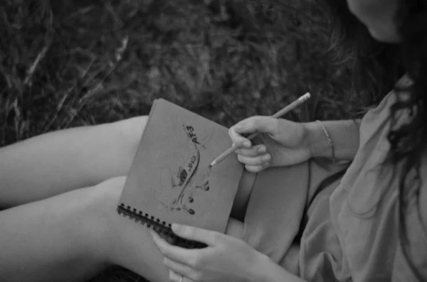 A young girl is drawing a plane in the sketchbook. Countryside photo with a girl who is drawing a picture. B&W photography.