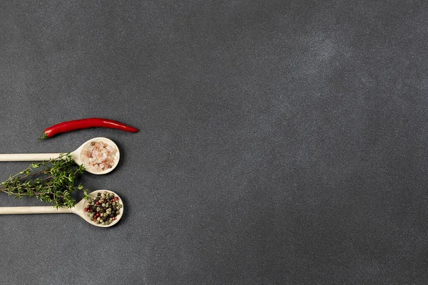 Wooden spoons with pink salt and pepper on the black background with copy space