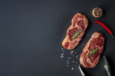 Kömür tahtasında baharatlı ve maşalı iki çiğ biftek..