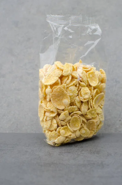 Transparent packaging with cornflakes on a gray background. Dry raw cereal.Crispy corn flakes in a transparent packageHealthy breakfast on the right diet, diet. Fitness breakfast