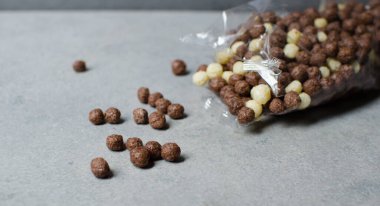 Gri bir zemine izole edilmiş çikolatalı mısır topları. Şeffaf ambalaj. Çiğ mısır gevreği. Şeffaf bir pakette gevrek. Spor kahvaltısı.
