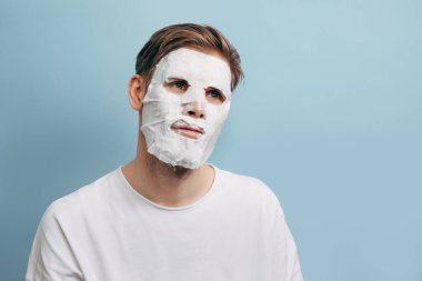 Erkek yüz bakımı. Mavi arka planda kozmetik kabarcık maskeli bir adam..