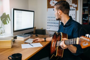 İnternet üzerinden gitar çalmayı öğrenen bir adam. Adam akustik gitar çalıyor. Coronavirus salgını sırasında evde konsept kal.