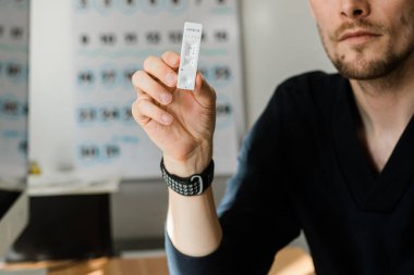 Riga, Letonya - 8 Nisan 2020: Evde ekspres koronavirüs testi. COVID-19 Coronavirus için hızlı test kaseti. Hızlı test kiti tutan bir adam. Kılavuz okuyan bir adam parmak izi testi nasıl yapılır?