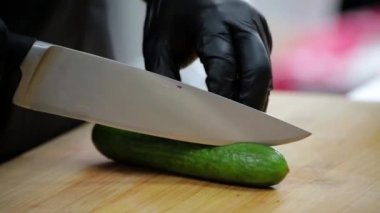 Aşçı kesme tahtasındaki keskin bir bıçakla salatalığı keser.