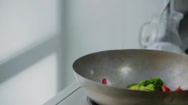 Şef, sebzeleri tavada ağır çekimde kızartıyor.