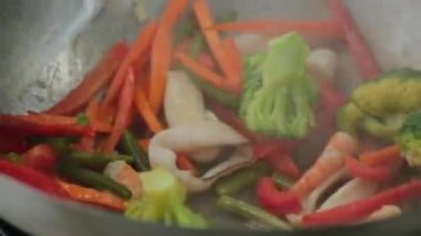 Şef tavada sebze, kalamar ve karides kızartıyor.