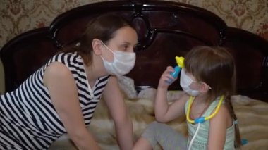 Anne ve bebek evde tıbbi maskelerle oynuyor. Kendini izole etmeyi karantinaya alıyorlar.