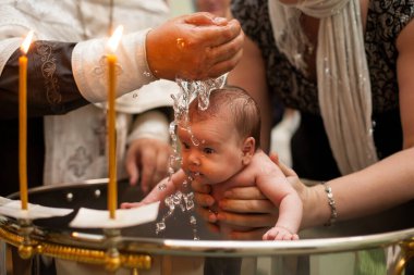 Kutsal suda yeni doğmuş bebek vaftiz töreni. Bebek annesinin elini tutuyor. Suda yıkanan bebek. Yazı tipinde vaftiz. Vaftiz ayini. Çocuk ve Tanrı. Vaftiz mumu. Kutsal su yazı tipi. Rahip vaftiz ediyor.