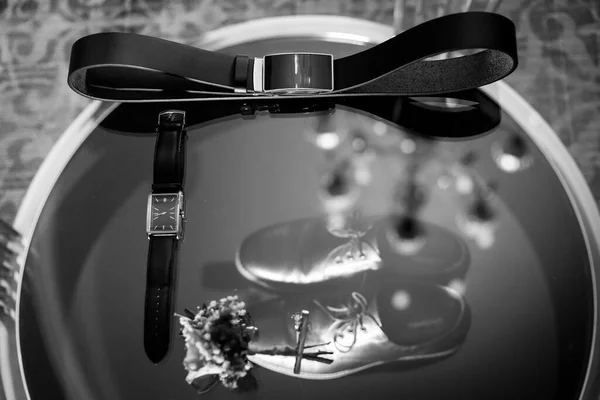 The groom is gathering in the morning. Wedding details on clear glass. Leather men's shoes with belt and bow tie. Set of groom accessories on wedding day. Black and white photo