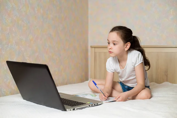 遠隔オンライン教育 デジタルタブレットノートパソコンで自宅で勉強し 学校の宿題をしている女子高生 トレーニング本と一緒にベッドに座って — ストック写真