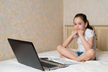 Uzaktan öğrenme çevrimiçi eğitim. Liseli kız evde dijital tablet dizüstü bilgisayarla ders çalışıyor ve okul ödevi yapıyor. Eğitim kitaplarıyla yatakta oturmak.