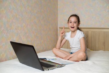 Uzaktan öğrenme çevrimiçi eğitim. Liseli kız evde dijital tablet dizüstü bilgisayarla ders çalışıyor ve okul ödevi yapıyor. Eğitim kitaplarıyla yatakta oturmak.