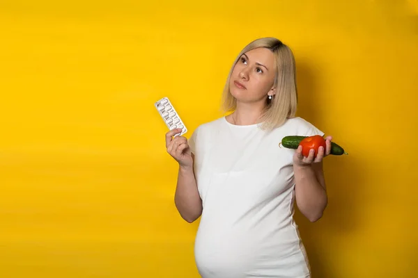 Een Zwangere Vrouw Kiest Tussen Pillen Groenten Een Gele Achtergrond — Stockfoto