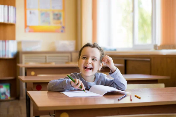 教室の机の上に座っていた白人の小さな笑顔の女の子は 純粋なノートに丁寧に描き始めます 幸せな弟子 — ストック写真