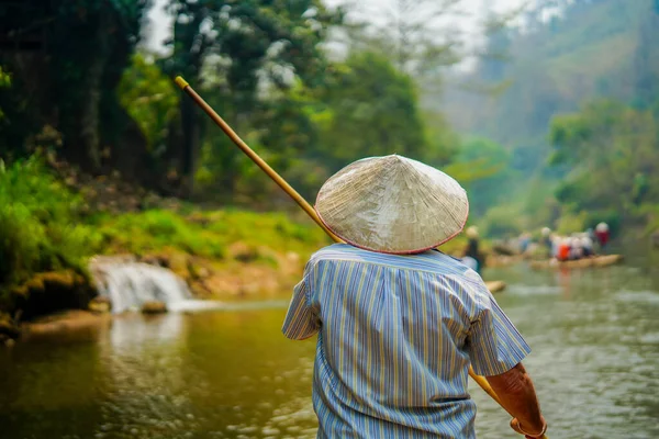 Chiang Mai, Tayland - 22 Mart 2019: Genç ahşap bot sürücüsü yeşil tepeler ve orman ormanları ile tropikal nehirde çubuk tutuyor