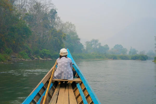 Yeşil ormandaki vahşi bir tropikal nehirde gezinen küçük ahşap bir tekne. Teknenin önünde bir kadın oturuyor ve manzarayı huzur içinde seyrediyor. Mavi kano doğayı keşfediyor..