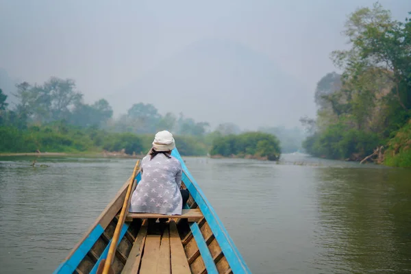 Small wooden boat navigating in a wild tropical river in the green jungle with a woman sitting in front of the boat and looking peacefully the scenery. Blue canoe exploring nature.