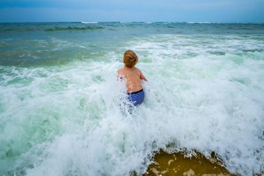 Neşeli çocuk tatillerde soğuk deniz suyuna giriyor. Neşeli ve neşeli çocuk sahilde eğleniyor. 