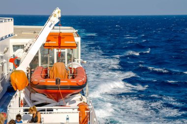 SANTORINI, GREECE - 22 HAZİRAN 2020: Mavi denizli daha büyük bir feribota bağlı Kızıl Hayat Gemisi